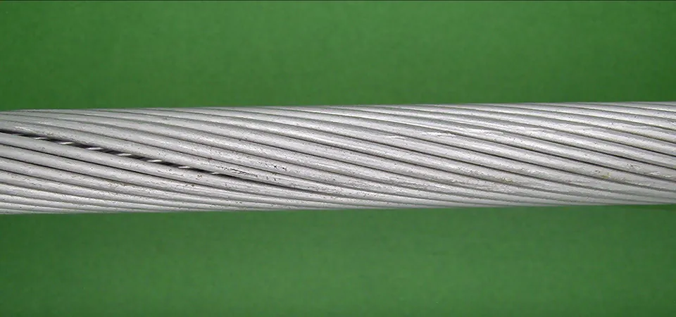A raw camera frame: a stranded aluminium cable crosses a green screen at a slight angle, with a dark groove where strands sit apart.